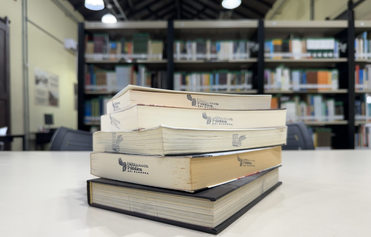 Pilha de livros da Biblioteca Pública Rui Barbosa sobre mesa de leitura em Jaraguá do Sul
