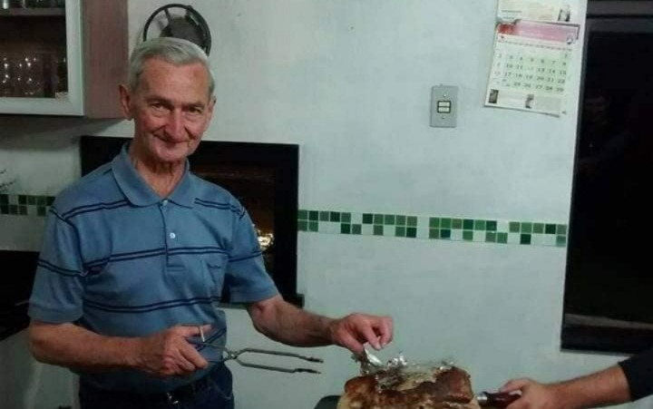 Osvaldo Oeschler sorri segurando utensílios de churrasco durante confraternização em família