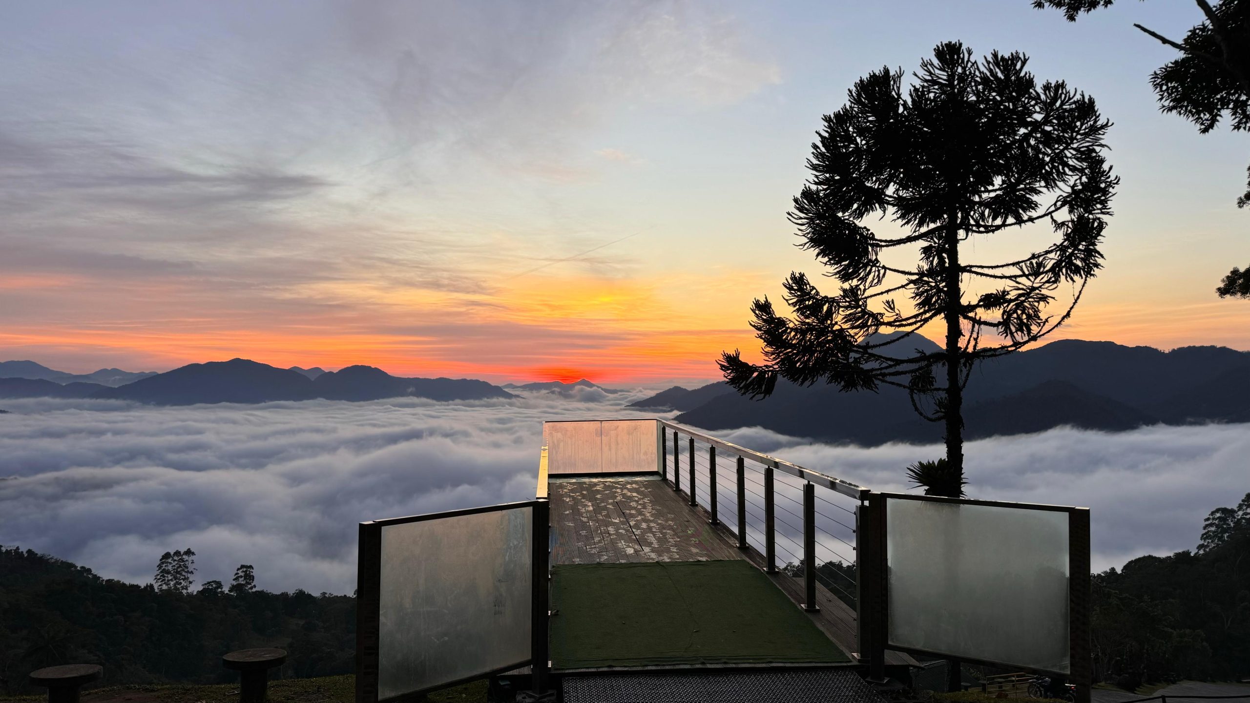 Mirante de vidro do Pico Malwee ao amanhecer com mar de nuvens e céu alaranjado