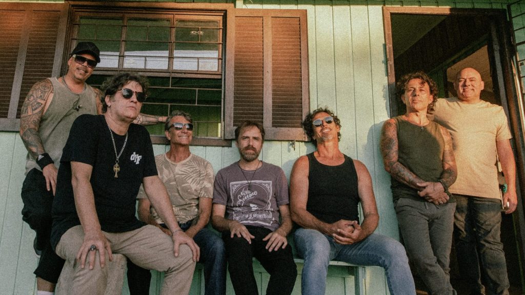 Integrantes do Dazaranha sentados em frente a uma casa com luz do pôr do sol