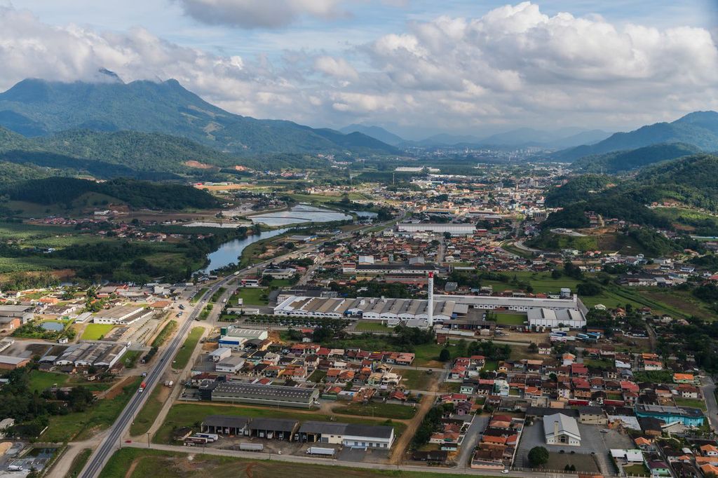 Imagem aérea de Guaramirim, mostrando áreas urbanas, industriais e paisagem natural ao redor da cidade.
