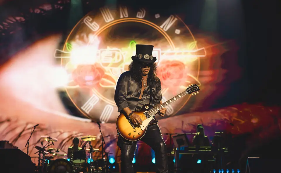 Slash toca guitarra em show do Guns N’ Roses com o logo da banda iluminado ao fundo