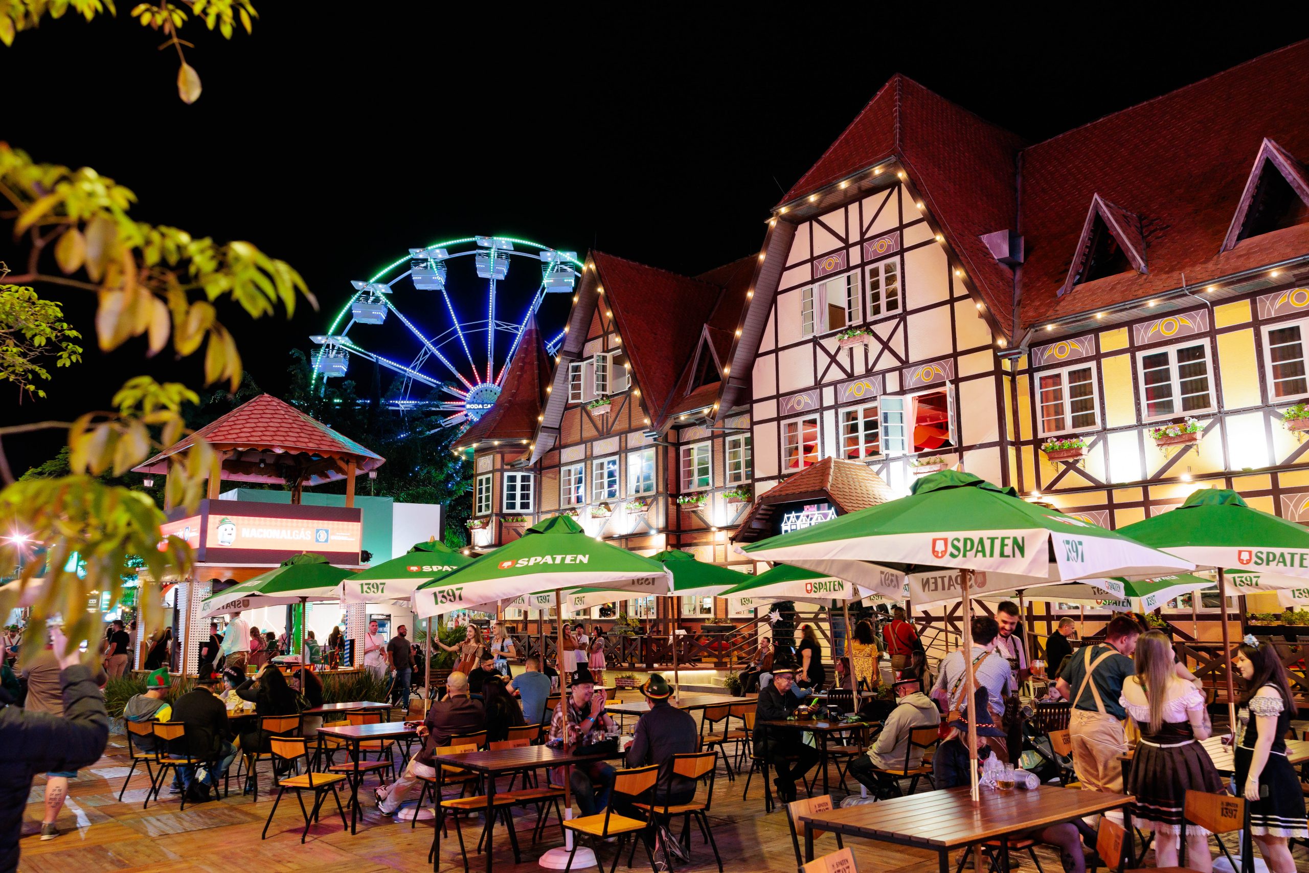 Público aproveita área externa da Oktoberfest Blumenau à noite com roda-gigante iluminada ao fundo