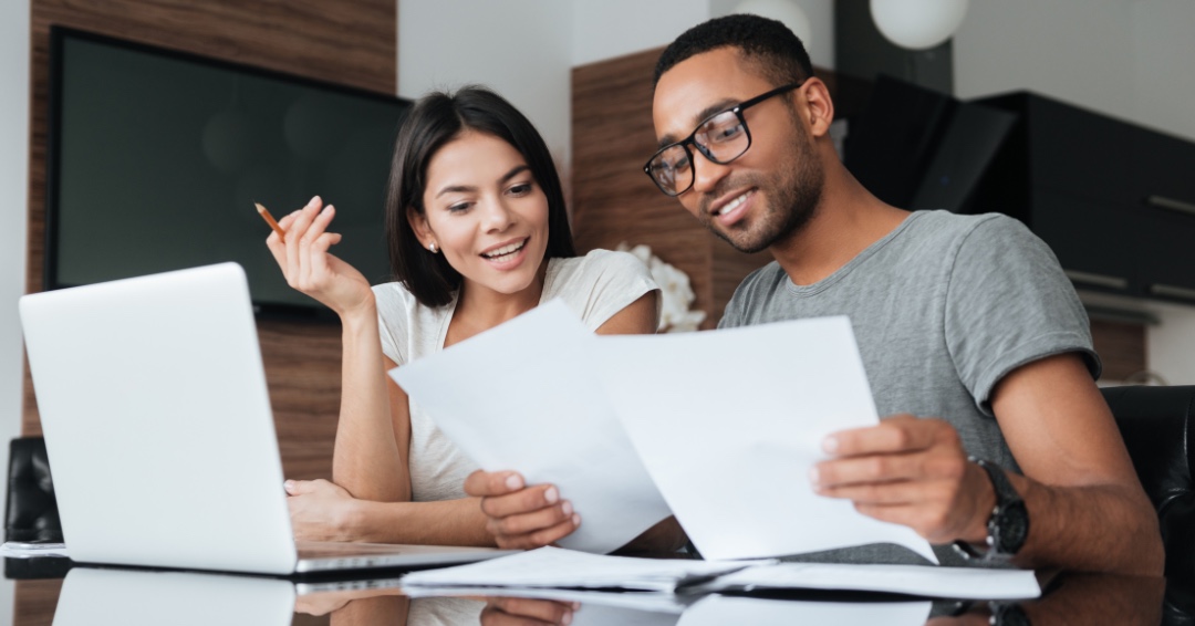 Casal sorridente revisa juntos documentos financeiros em casa