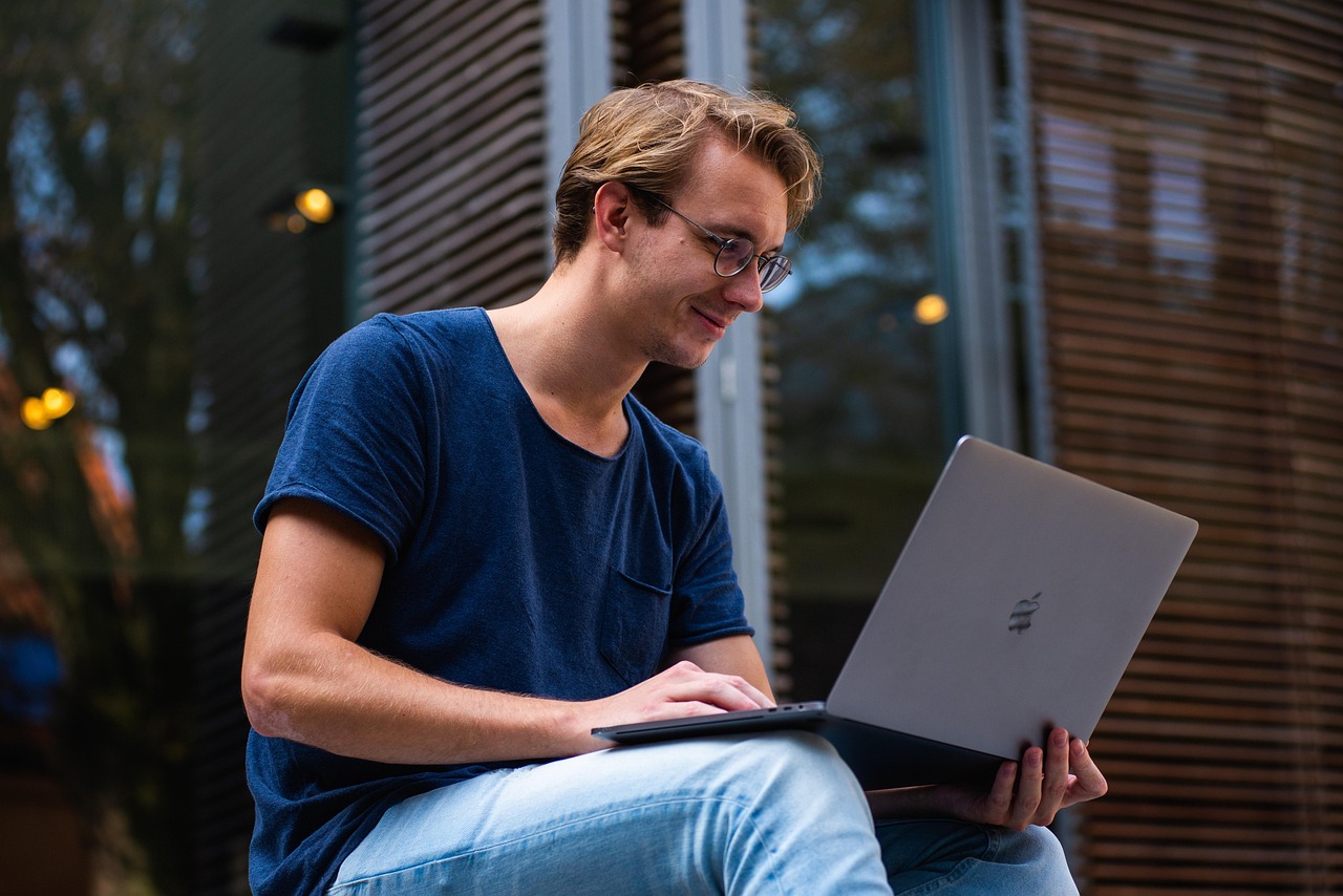 Jovem sentado ao ar livre usando notebook para estudo online em ambiente urbano
