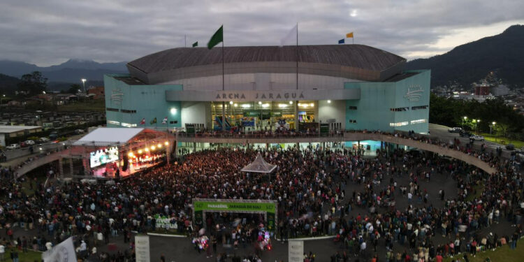 Multidão reunida em frente à Arena Jaraguá durante show de aniversário da cidade