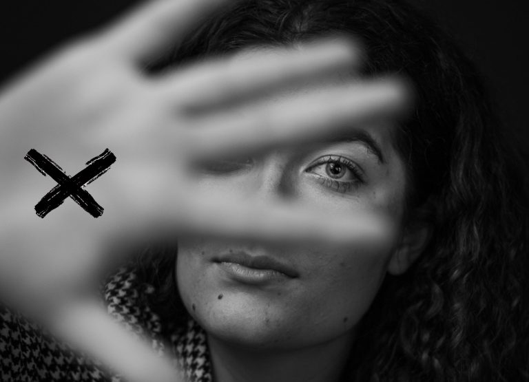 Mulher mostra a palma da mão com um X desenhado, símbolo do sinal vermelho contra violência